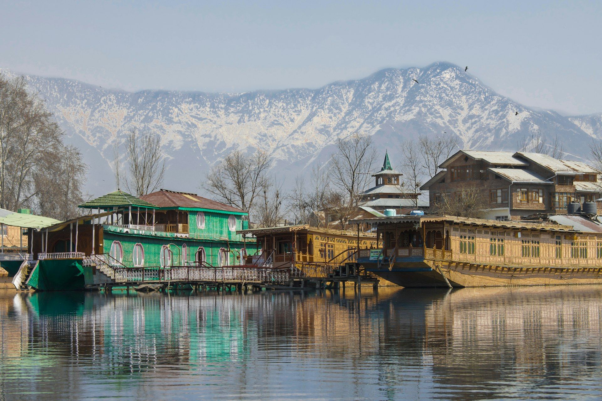 Wooden houseboats on Dal Lake in Srinagar, with snow-covered mountains behind.